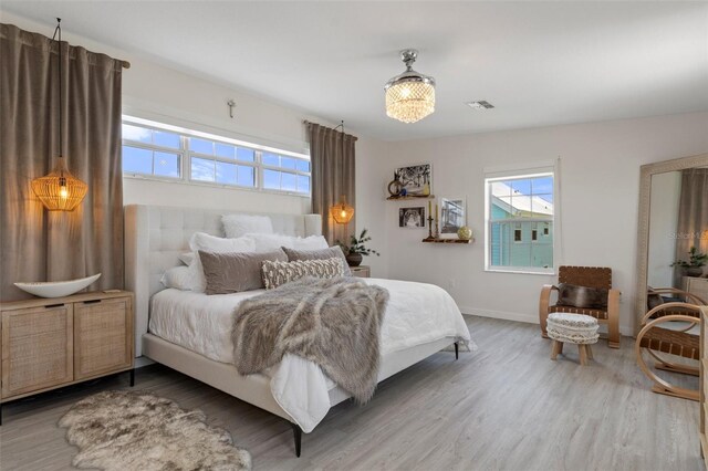 bedroom featuring multiple windows, wood finished floors, baseboards, and a chandelier