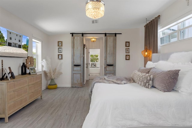 bedroom with light wood-style floors, multiple windows, a barn door, and a chandelier