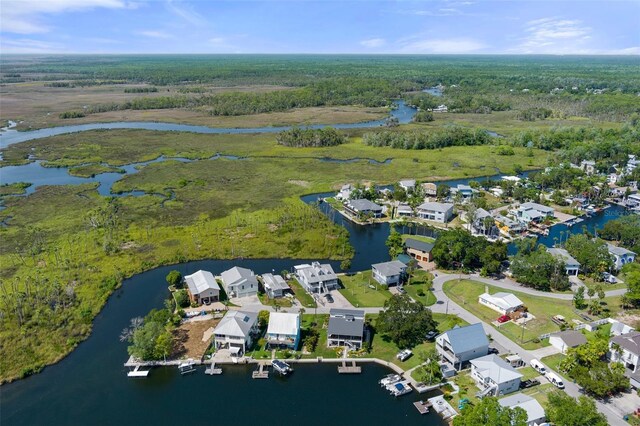 aerial view of property and surrounding area featuring a nearby body of water, a heavily wooded area, and nearby suburban area