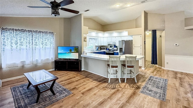 kitchen with stainless steel appliances, lofted ceiling, light wood-style flooring, a peninsula, and ceiling fan