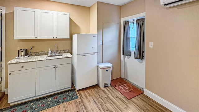 kitchen with freestanding refrigerator, a sink, light wood-style floors, a wall mounted air conditioner, and white cabinets