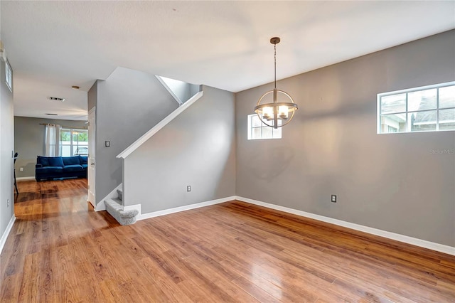 unfurnished dining area with stairs, light wood-type flooring, baseboards, and a chandelier