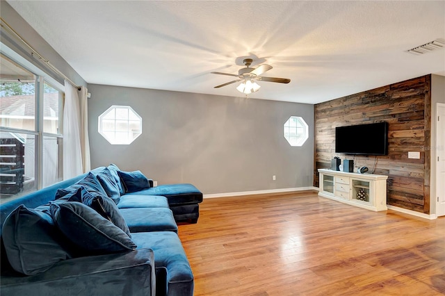 living room with a ceiling fan, baseboards, light wood-style floors, and an accent wall