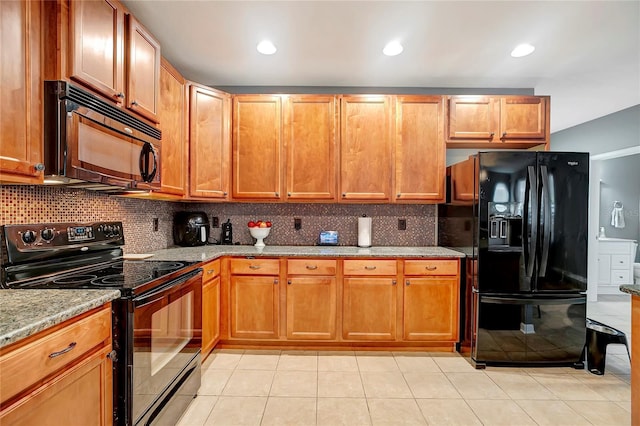 kitchen featuring black appliances, decorative backsplash, light stone countertops, light tile patterned floors, and brown cabinetry