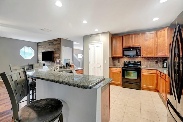 kitchen featuring black appliances, a sink, a breakfast bar area, backsplash, and light tile patterned floors