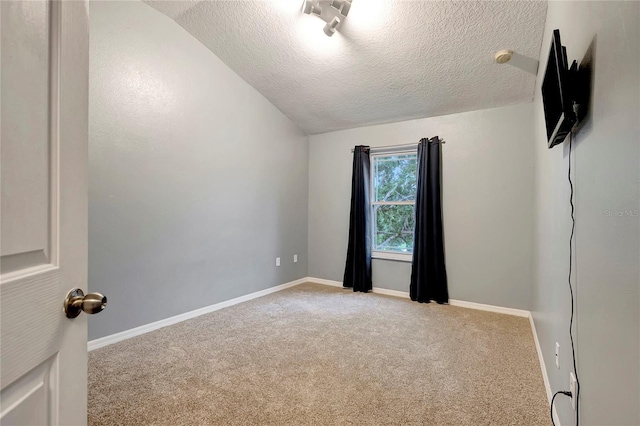 spare room featuring a textured ceiling, carpet floors, vaulted ceiling, and baseboards