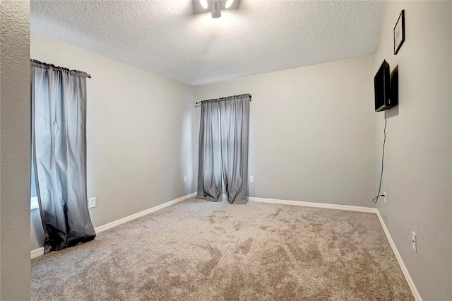 spare room with a textured ceiling, carpet, and baseboards