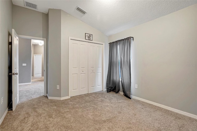 unfurnished bedroom with light carpet, vaulted ceiling, a closet, baseboards, and a textured ceiling
