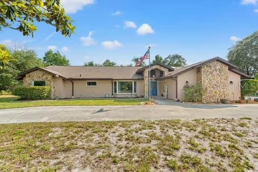 5216 Hope Ln, Spring Hill, FL 34606 - view of front of property with stone siding, a front lawn, driveway, and stucco siding