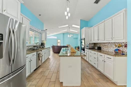 5216 Hope Ln, Spring Hill, FL 34606 - kitchen with appliances with stainless steel finishes, a kitchen island, tasteful backsplash, white cabinets, and vaulted ceiling