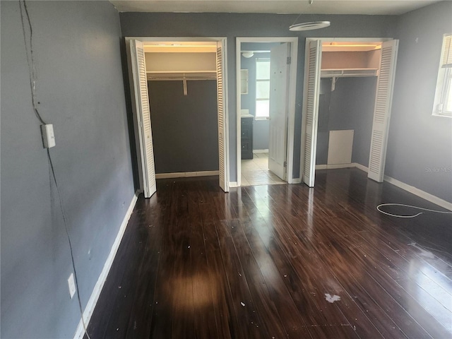 unfurnished bedroom with hardwood / wood-style floors, baseboards, and two closets