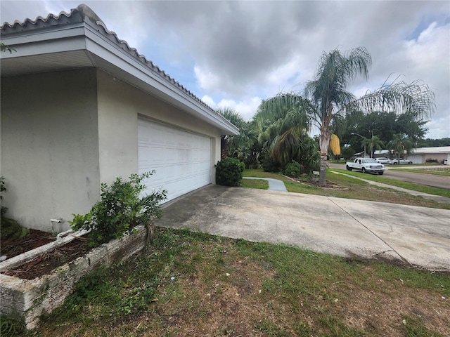 view of side of property with stucco siding, concrete driveway, a tiled roof, and a lawn