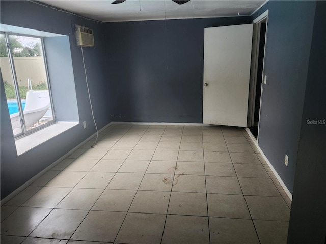 empty room with a ceiling fan, a wall unit AC, tile patterned flooring, and baseboards