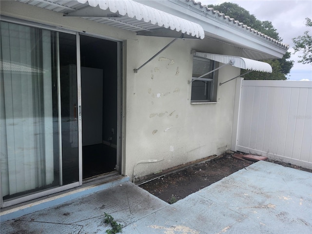 view of exterior entry with fence and stucco siding