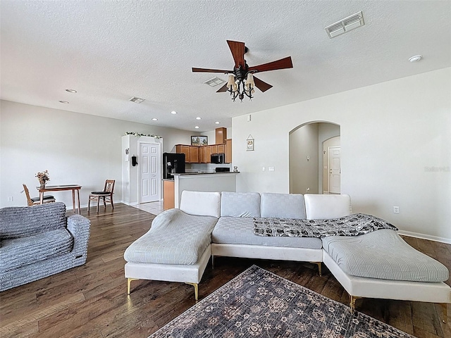 living area featuring arched walkways, a ceiling fan, wood finished floors, baseboards, and a textured ceiling