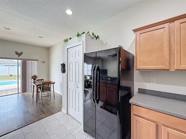 kitchen featuring black refrigerator with ice dispenser, a textured ceiling, dark countertops, light tile patterned floors, and recessed lighting