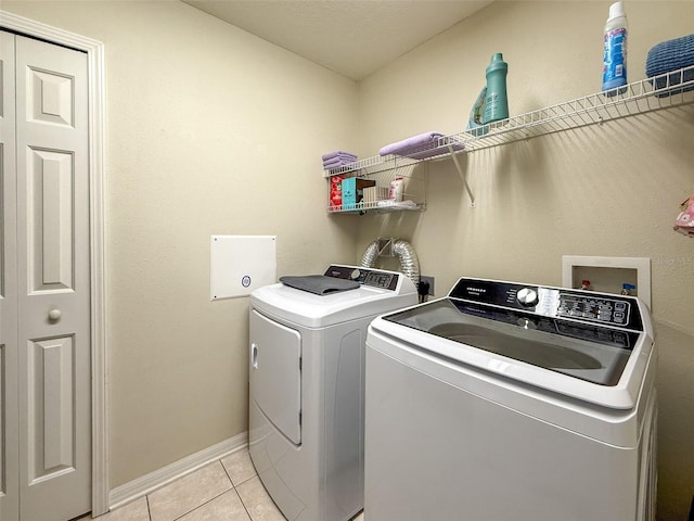 clothes washing area featuring washer and dryer, light tile patterned flooring, and baseboards