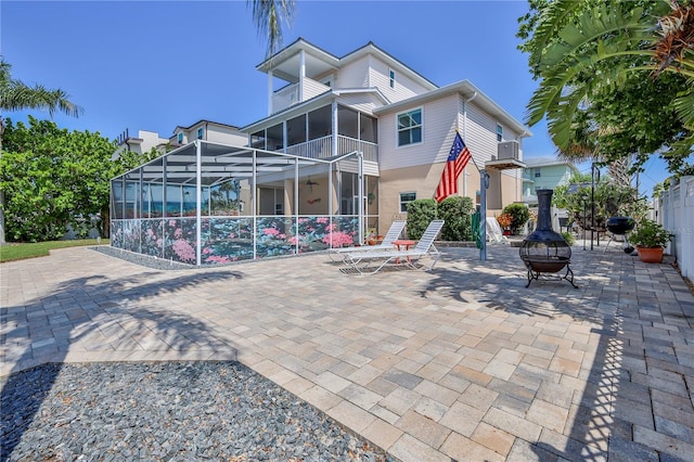 back of property featuring a patio, a fire pit, glass enclosure, and a balcony