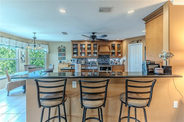 kitchen with custom range hood, brown cabinets, dark countertops, ceiling fan, and decorative backsplash