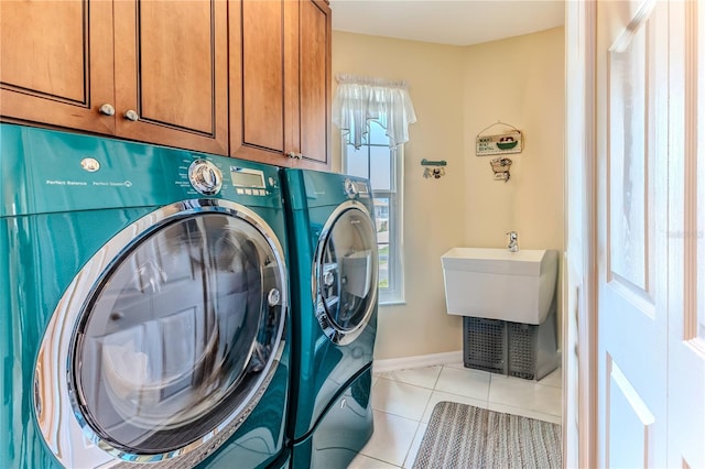 clothes washing area with washing machine and clothes dryer, cabinet space, light tile patterned floors, and baseboards