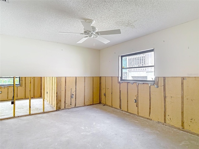 4420 Marine Pkwy, New Port Richey, FL 34652 - unfurnished room featuring plenty of natural light, a ceiling fan, unfinished concrete floors, a textured ceiling, and a wainscoted wall