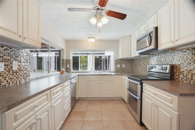 12106 Bear Creek Ln, Hudson, FL 34667 - kitchen featuring stainless steel appliances, a sink, decorative backsplash, light tile patterned floors, and dark countertops