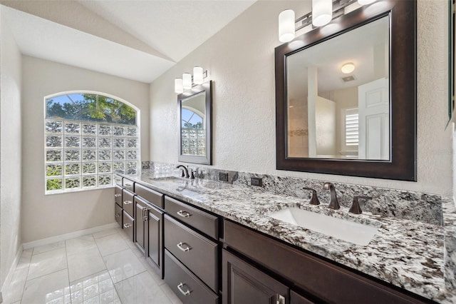 full bath featuring vaulted ceiling, baseboards, and double vanity