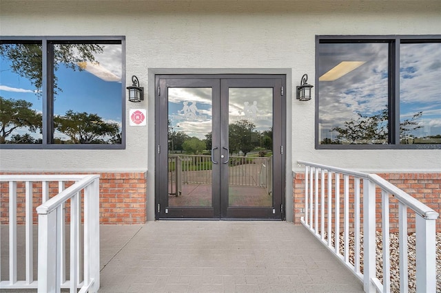 view of exterior entry with french doors, stucco siding, and brick siding