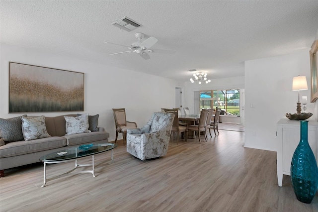 living area with light wood-style floors, a textured ceiling, a ceiling fan, and a chandelier