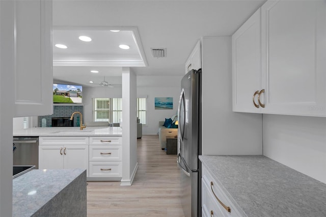 kitchen with a sink, stainless steel appliances, light wood finished floors, a raised ceiling, and recessed lighting