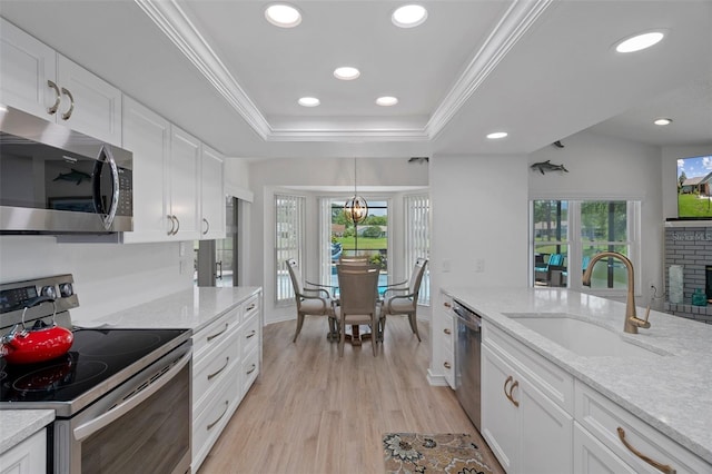 kitchen featuring stainless steel appliances, a sink, ornamental molding, white cabinets, and light wood-style flooring