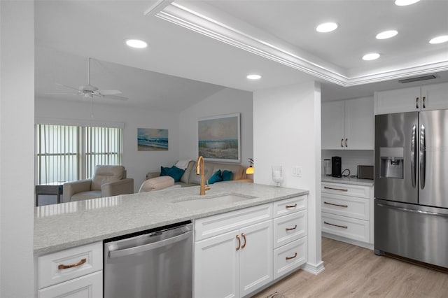 kitchen with appliances with stainless steel finishes, a sink, light wood-style floors, a ceiling fan, and light stone countertops