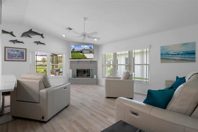 living area featuring a ceiling fan, a textured ceiling, a brick fireplace, plenty of natural light, and lofted ceiling