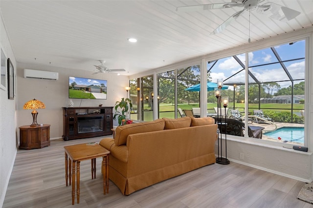 living room featuring a ceiling fan, a sunroom, a wall unit AC, and wood finished floors