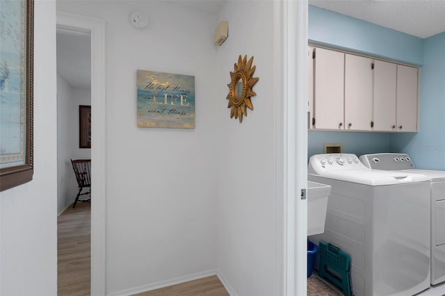 laundry room with cabinet space, washing machine and clothes dryer, light wood finished floors, baseboards, and a textured ceiling