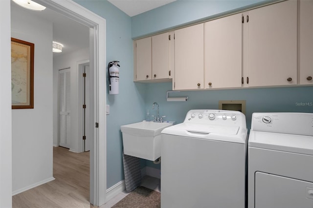 washroom featuring cabinet space, washing machine and dryer, baseboards, and light wood-style flooring