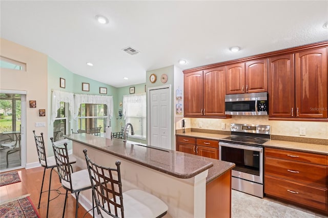 12071 Wexford Blvd, Spring Hill, FL 34609 - kitchen with stainless steel appliances, vaulted ceiling, a kitchen bar, an island with sink, and dark stone counters