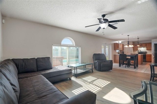 living area with a ceiling fan, a chandelier, a textured ceiling, and light wood-style flooring