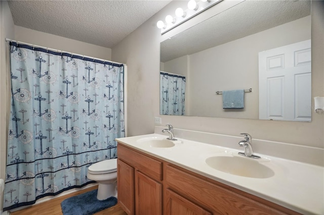 bathroom with toilet, wood finished floors, double vanity, a textured ceiling, and curtained shower