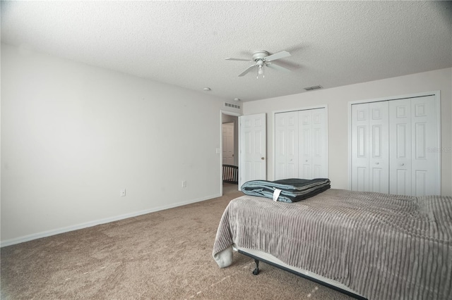 bedroom with carpet, two closets, baseboards, ceiling fan, and a textured ceiling