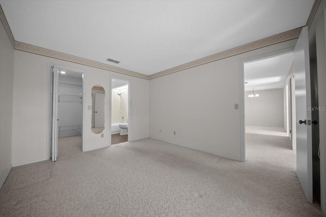 unfurnished bedroom featuring light colored carpet, a walk in closet, ensuite bathroom, and a closet