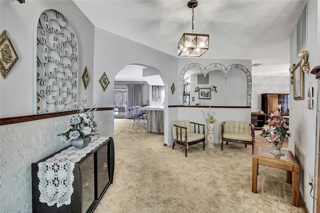 corridor with light carpet, a textured ceiling, a chandelier, and arched walkways