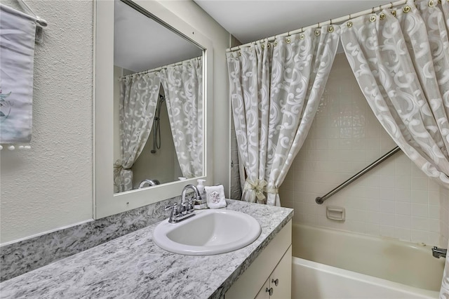 full bath with a textured wall, vanity, and shower / tub combo
