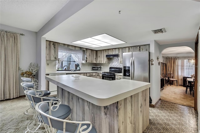 kitchen with black gas stove, arched walkways, light countertops, under cabinet range hood, and light colored carpet