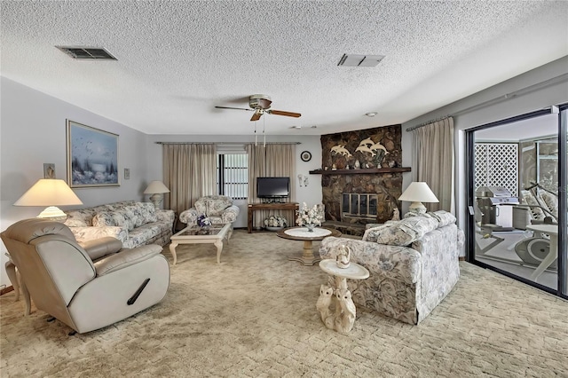 living area with a ceiling fan, a textured ceiling, carpet, and a stone fireplace