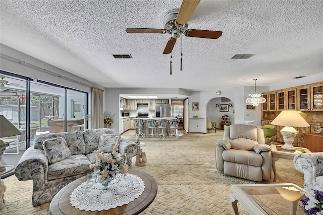 living room featuring a ceiling fan, a textured ceiling, arched walkways, and light carpet