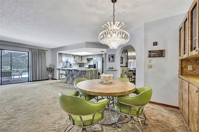 dining space featuring arched walkways, a chandelier, a textured ceiling, light carpet, and baseboards
