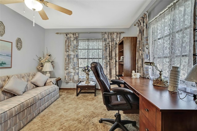 carpeted office space featuring a ceiling fan and baseboards