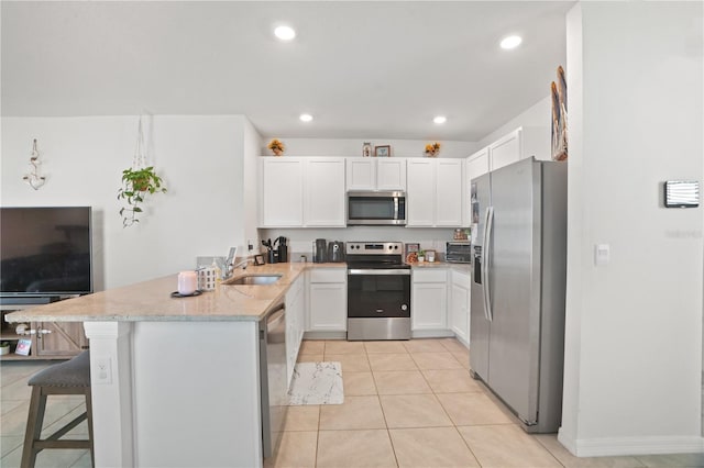 kitchen featuring appliances with stainless steel finishes, a peninsula, a sink, white cabinets, and light stone countertops