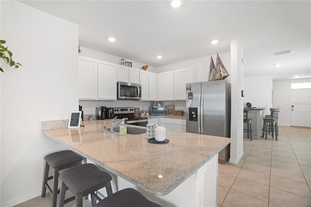 kitchen featuring appliances with stainless steel finishes, a peninsula, a sink, a kitchen breakfast bar, and light stone countertops